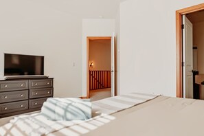 A bedroom with a bed, a dresser, a television, and a door leading to a staircase.