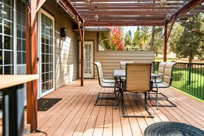 A covered patio with a table and chairs, a wooden deck, and a view of a yard with trees.