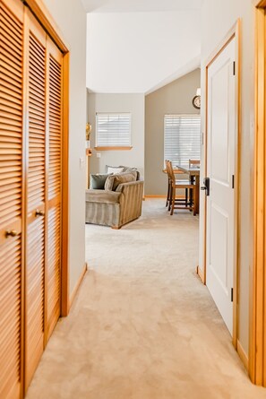 A hallway leading to a living area with a sofa, a dining table, and a clock on the wall.