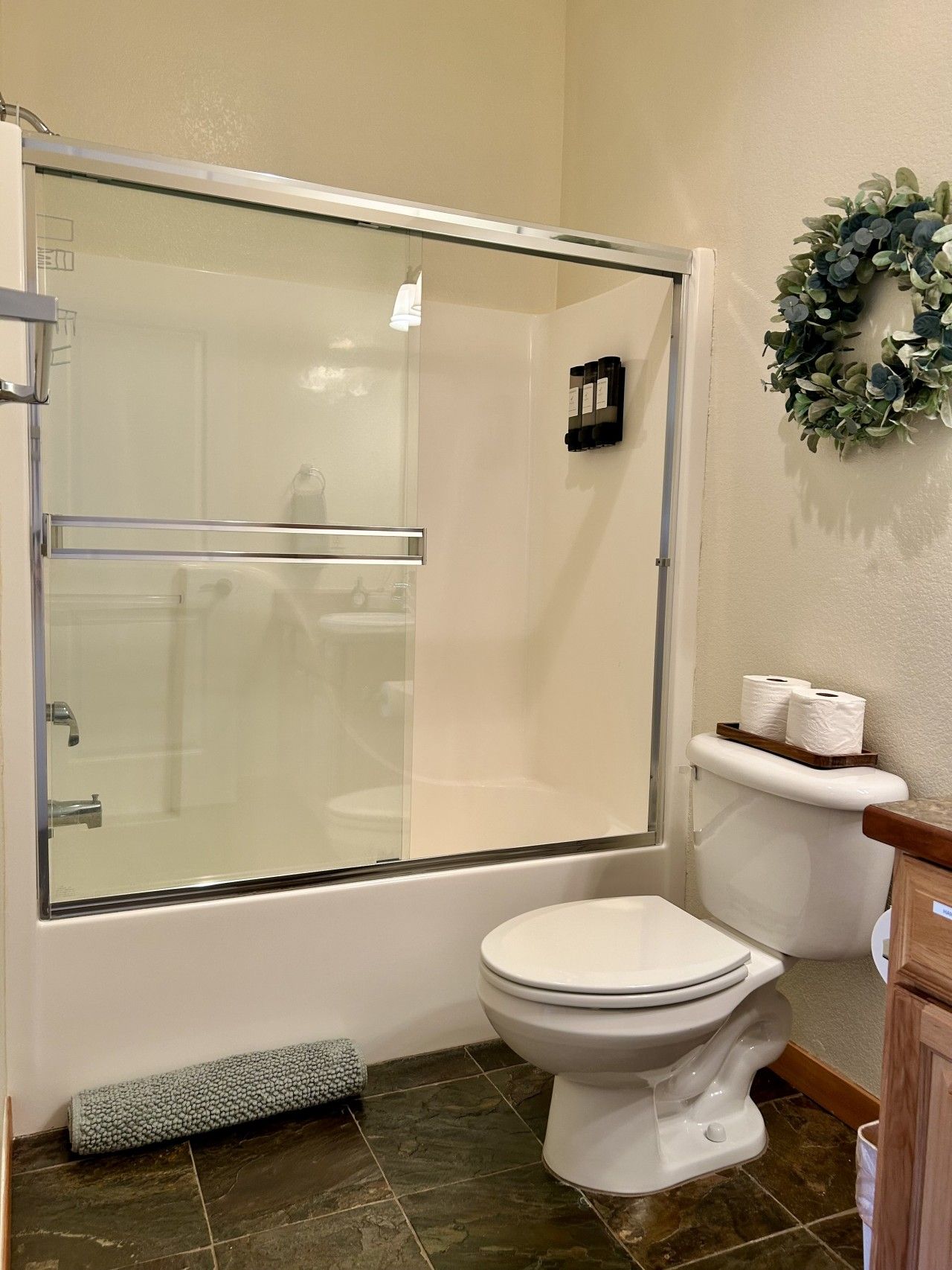 Une salle de bain avec une douche à parois de verre, des toilettes et une petite étagère avec du papier toilette.