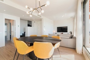 A modern dining area with a round table and yellow chairs, a sofa, a flat-screen TV, and a staircase leading to another room. - LM352B- Spacious duplex penthouse with panoramic (Estepona)