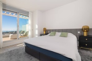 A bedroom with a large bed, two bedside tables, a view through a sliding glass door, and a chair by the window. - LM352B- Spacious duplex penthouse with panoramic (Estepona)