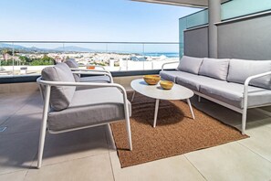 Varanda moderna com sofá, poltrona e mesa redonda, com vista para a cidade.