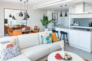 A modern living room with a sofa, a dining area, and a kitchen with bar stools. - Estepona Penthouse, Hot Tub, Views Oasis325 (Málaga)