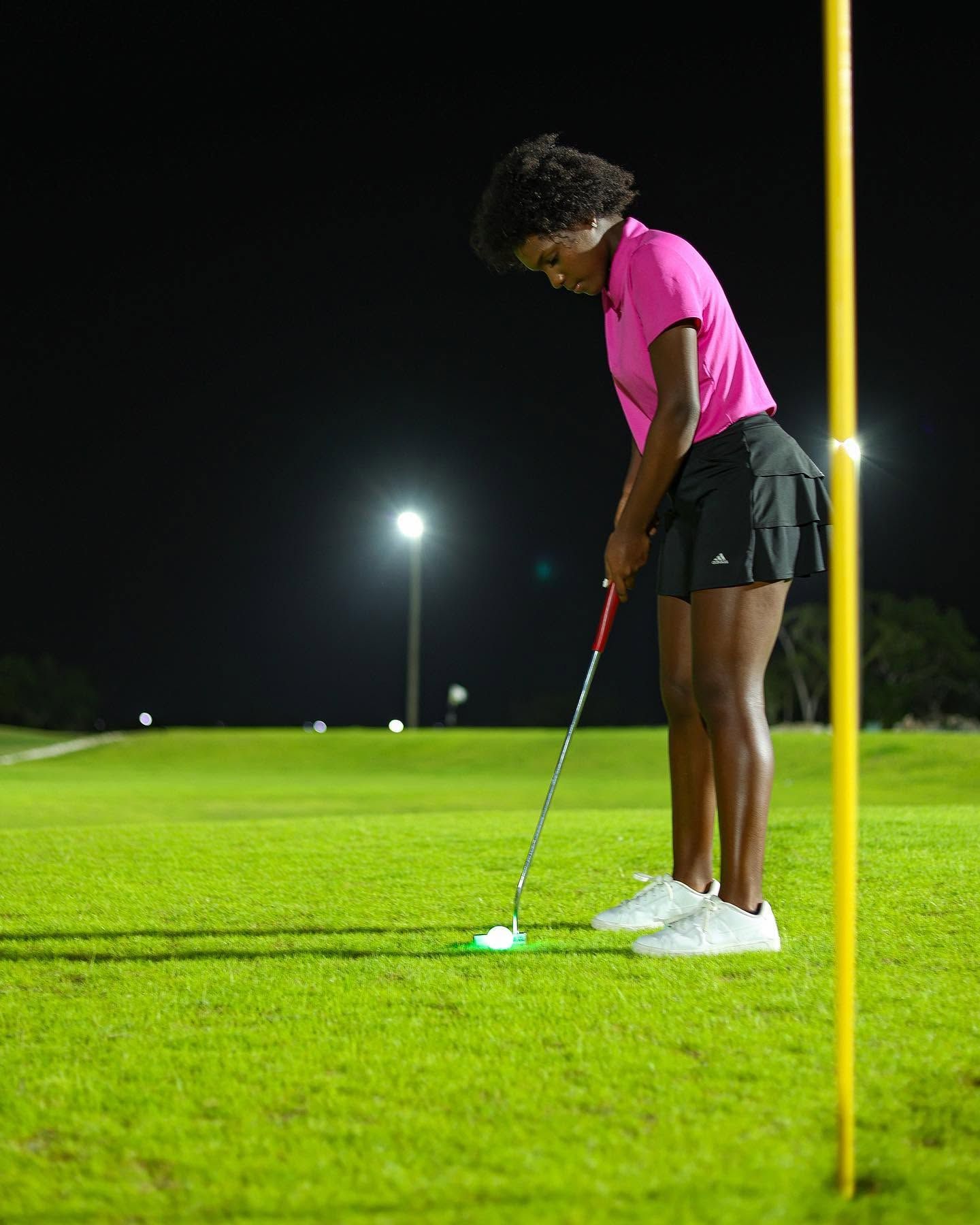 Eine Person spielt nachts Golf, beleuchtet durch künstliches Licht.