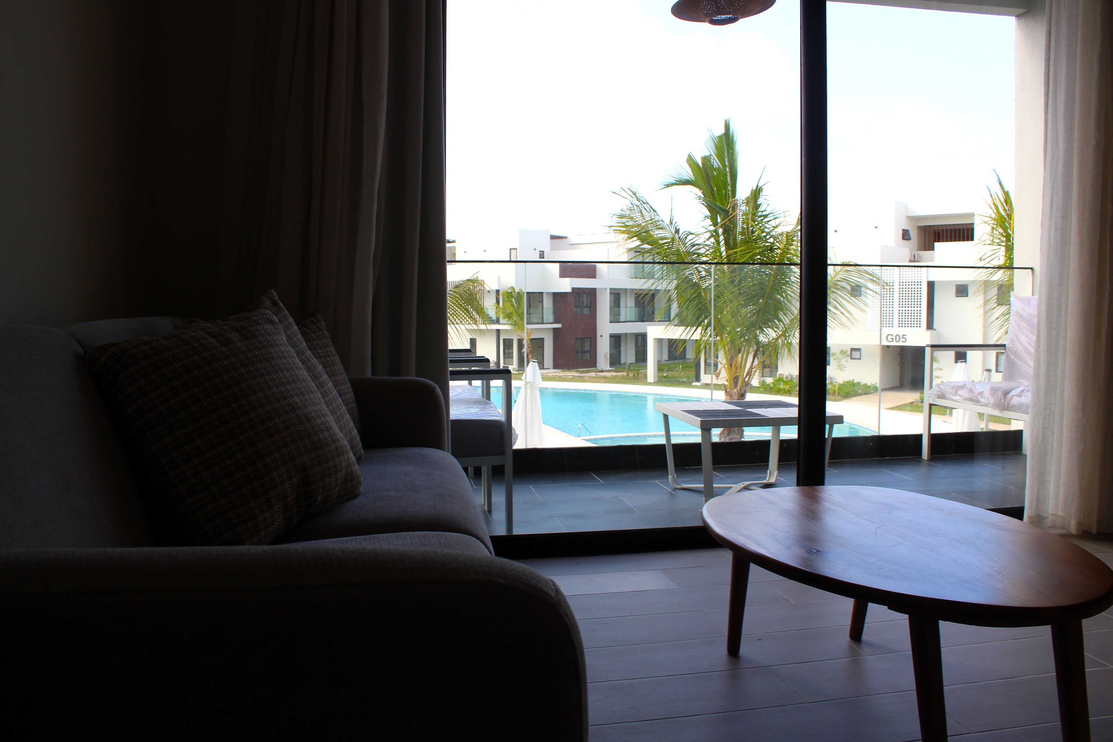 Quarto com sofá, uma mesa pequena e vista para uma piscina e edifícios.