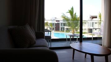 Quarto com sofá, uma mesa pequena e vista para uma piscina e edifícios.