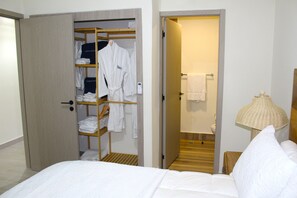 Ett hotellrum med en säng, en garderob med upphängningsmöjligheter för kläder, ett badrum med en handduksställning och en sänglampa.