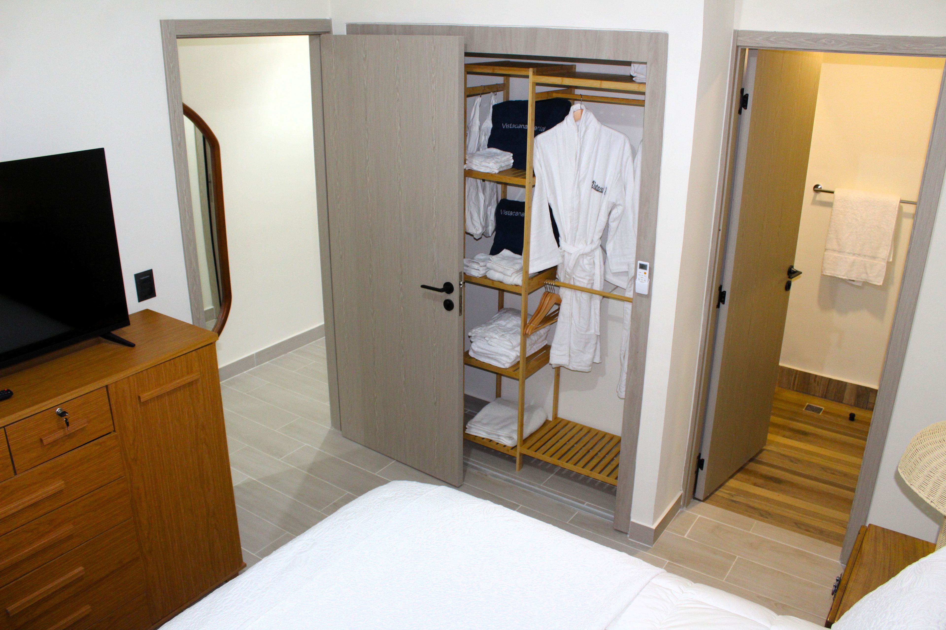 Une chambre d’hôtel comprenant un lit, une commode en bois, un placard avec des vêtements suspendus et un téléviseur.