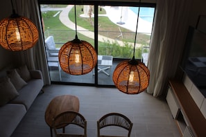 Ein modernes Wohnzimmer mit einer Couch, zwei Sesseln und einem großen Fenster mit Blick auf Garten und Pool.