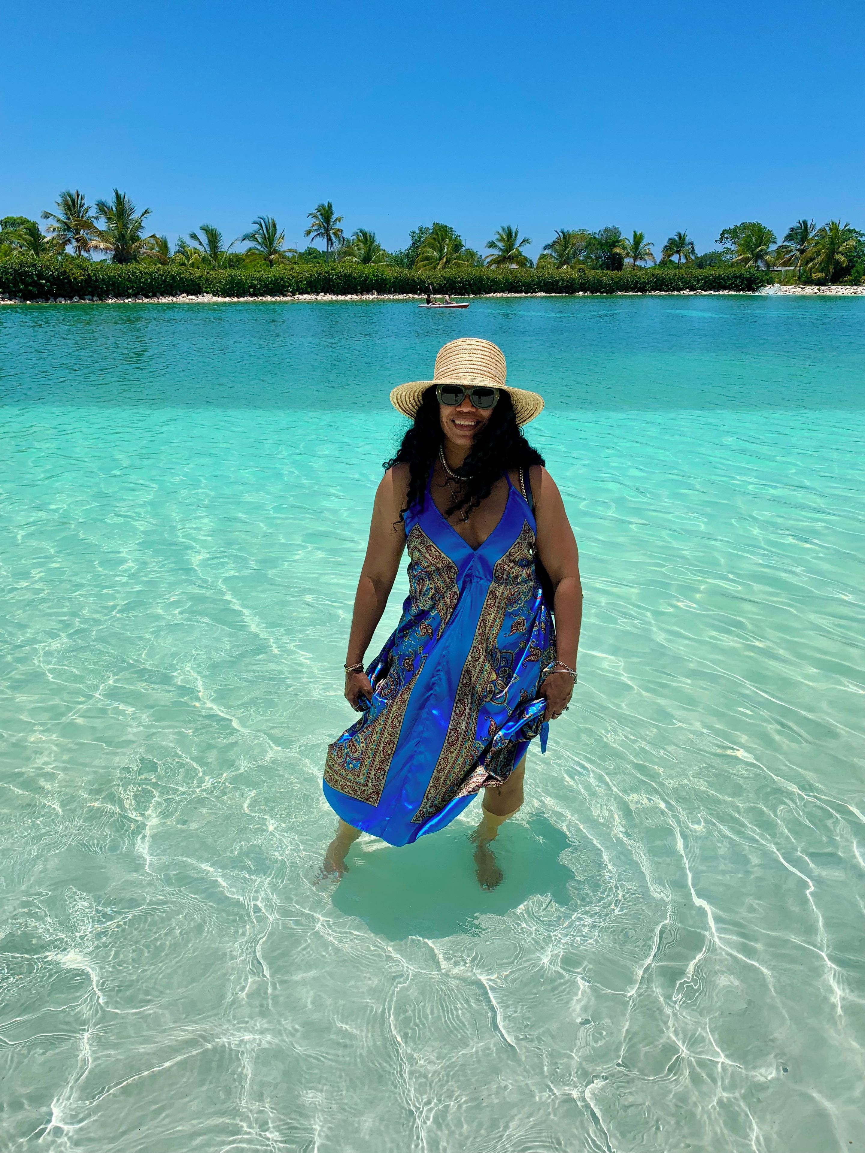 A person standing in clear turquoise water with a beach and palm trees in the background.