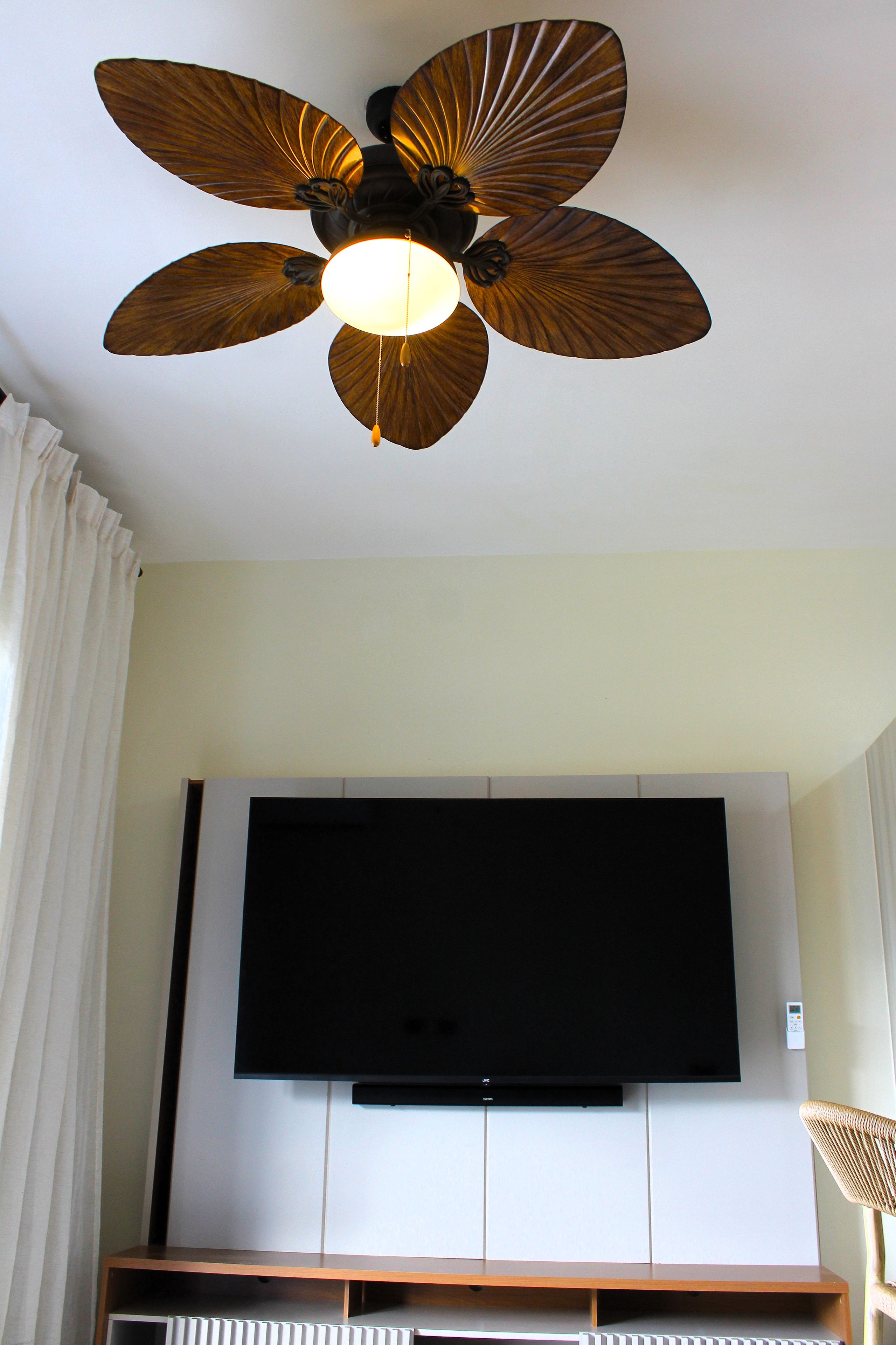 Ein Deckenventilator mit Leuchte und ein Flachbildfernseher an der Wand.