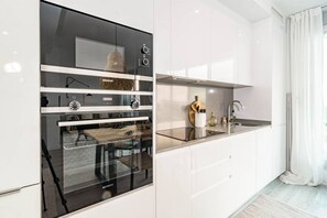 Et moderne køkken med indbygget ovn, bordplade i rustfrit stål og en hængende pendel.