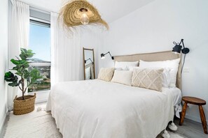 A bedroom with a large bed, a bedside table, a lamp, a hanging light fixture, a potted plant, and a view of the outside. - OV - Stunning flat in resort (Estepona)
