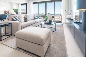Ein modernes Wohnzimmer mit Sofa, Hocker, Couchtisch und Meerblick.