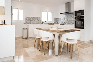 Een moderne keuken met witte kasten, een marmeren spatwand en een eetgedeelte met een houten tafel en witte stoelen.