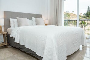 Een slaapkamer met een groot bed, twee nachtkastjes met lampen, een balkon met een hekwerk en uitzicht op de omgeving.