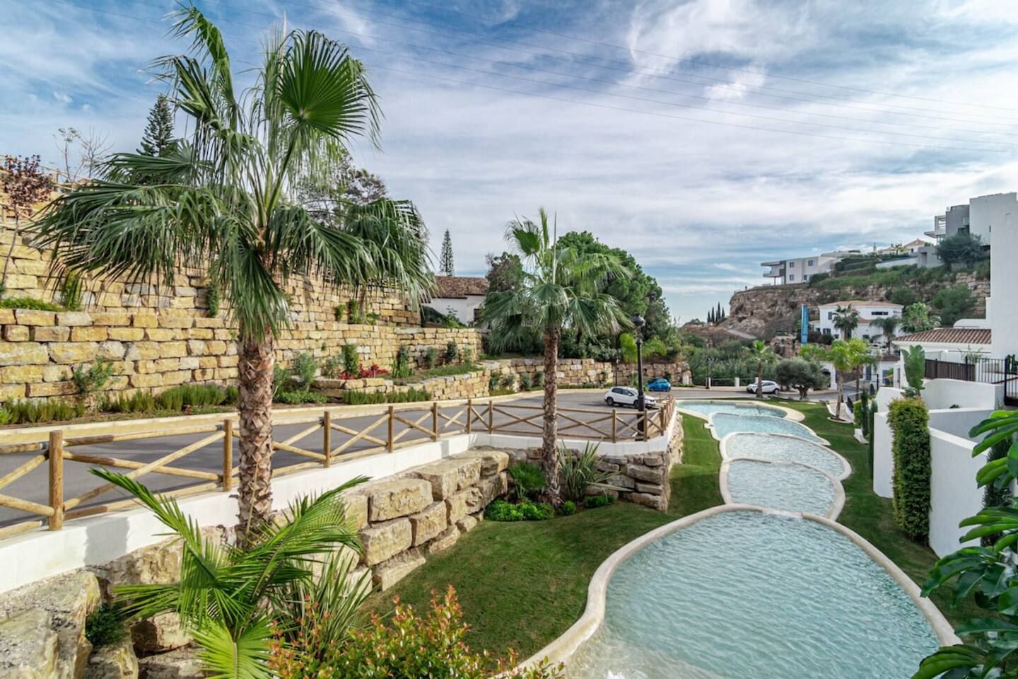 Un complexe hôtelier doté d’une piscine, de palmiers et d’un mur en pierre.