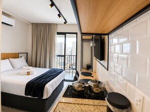 A hotel room with a bed, a small kitchenette, a TV, and a balcony with a view of the city. - SETIN 1903 (São Paulo)
