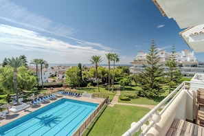 A swimming pool with lounge chairs, surrounded by greenery and buildings in the background. - RG133 - Spacious 3 bed apartment in prime location (Marbella)