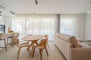 A modern living room with a round wooden table and chairs, a beige sofa, and large windows with sheer curtains. - SA59 - Elegant semi-detached house with solarium (Estepona)