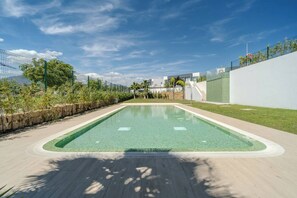 Ein rechteckiger Pool mit Fliesenrand, umgeben von einer Holzterrasse und einer niedrigen Steinmauer.