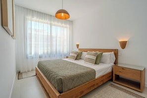 Ein Schlafzimmer mit einem hölzernen Bett, weißer Bettwäsche, einer grünen Tagesdecke, einem Nachttisch und einer wandmontierten Lampe.