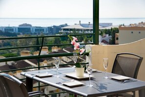 Ein Esstisch für zwei Personen, mit Blick auf das Meer und Gebäude im Hintergrund.