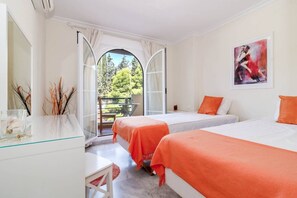 A hotel room with two beds, a desk, a chair, and a large window offering a view of trees. - SAA- Comfortable Apartment near Puerto Banus (Marbella)