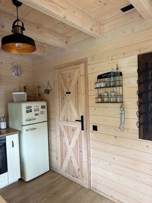 Una cocina con un refrigerador blanco, paredes de madera, una lámpara colgante, un reloj y un especiero instalado en la pared.