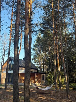 A modern house surrounded by tall trees, with a hammock in the yard. - Modern Barn with SPA, 5 km from Zegrze Reservoir (Beniaminów)