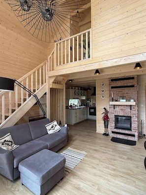 A spacious living area with a grey sofa, a staircase, a kitchen, and a fireplace. - Modern Barn with SPA, 5 km from Zegrze Reservoir (Beniaminów)