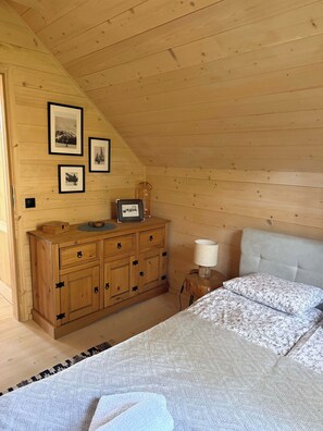 A bedroom with a wooden headboard, a bed with patterned bedding, a wooden dresser with drawers, and framed pictures on the wall. - Modern Barn with SPA, 5 km from Zegrze Reservoir (Beniaminów)
