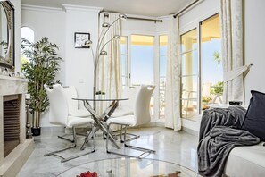 A modern living room with a glass table, white chairs, a sofa, and a view of the outdoors. - SAA2- comfortable apartment Puerto banus (Marbella)