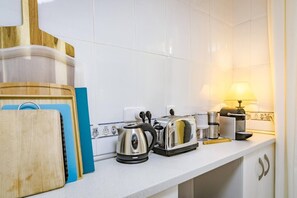 Una cocina con azulejos blancos, un tostador, un hervidor y una cafetera sobre la encimera.