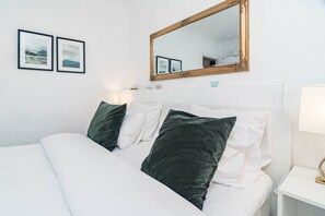 A bed with white bedding and dark green pillows, a bedside table with a lamp, and a wall-mounted mirror. - SAT2 - Modern 2 bedroom apartment with ocean view (Marbella)