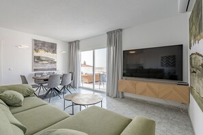 A modern living room with a sofa, dining table, chairs, and a large TV. - ILIVE Villa with Ocean Views and a Heated Pool in Sueño Azul (Callao Salvaje)