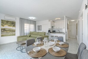 A modern living room with a green sofa, dining table set with white bowls and glasses, and a kitchen in the background. - ILIVE Villa with Ocean Views and a Heated Pool in Sueño Azul (Callao Salvaje)