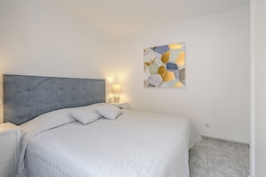 A neatly made bed with a grey headboard, a bedside table with a lamp, and a wall-mounted abstract art piece. - ILIVE Villa with Ocean Views and a Heated Pool in Sueño Azul (Callao Salvaje)
