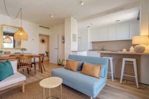 A modern living room with a sofa, a dining table, and a kitchen area with white cabinets. - New modern apt, rooftop pool, Estepona - zaga3c (Estepona)