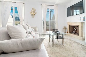A modern living room with a sofa, a glass coffee table, a fireplace, and a TV mounted on the wall. - SAT25i Penthouse with Sea Views in Nueva Andalucia (Marbella)