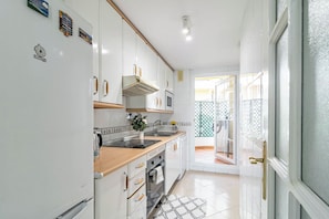 A compact kitchen with white cabinets, a stove, and a sink. There is a small window and a door leading to a balcony. - SAT25i Penthouse with Sea Views in Nueva Andalucia (Marbella)