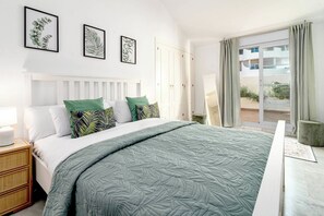 A hotel room with a bed, a nightstand, a window with curtains, and framed botanical prints on the wall. - SAT25i Penthouse with Sea Views in Nueva Andalucia (Marbella)