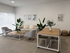 A modern living room with a sofa, two coffee tables, and chairs. There are plants on the tables and a wall with framed pictures. - SB311G - Modern & well connected 2 bed apartment (Estepona)