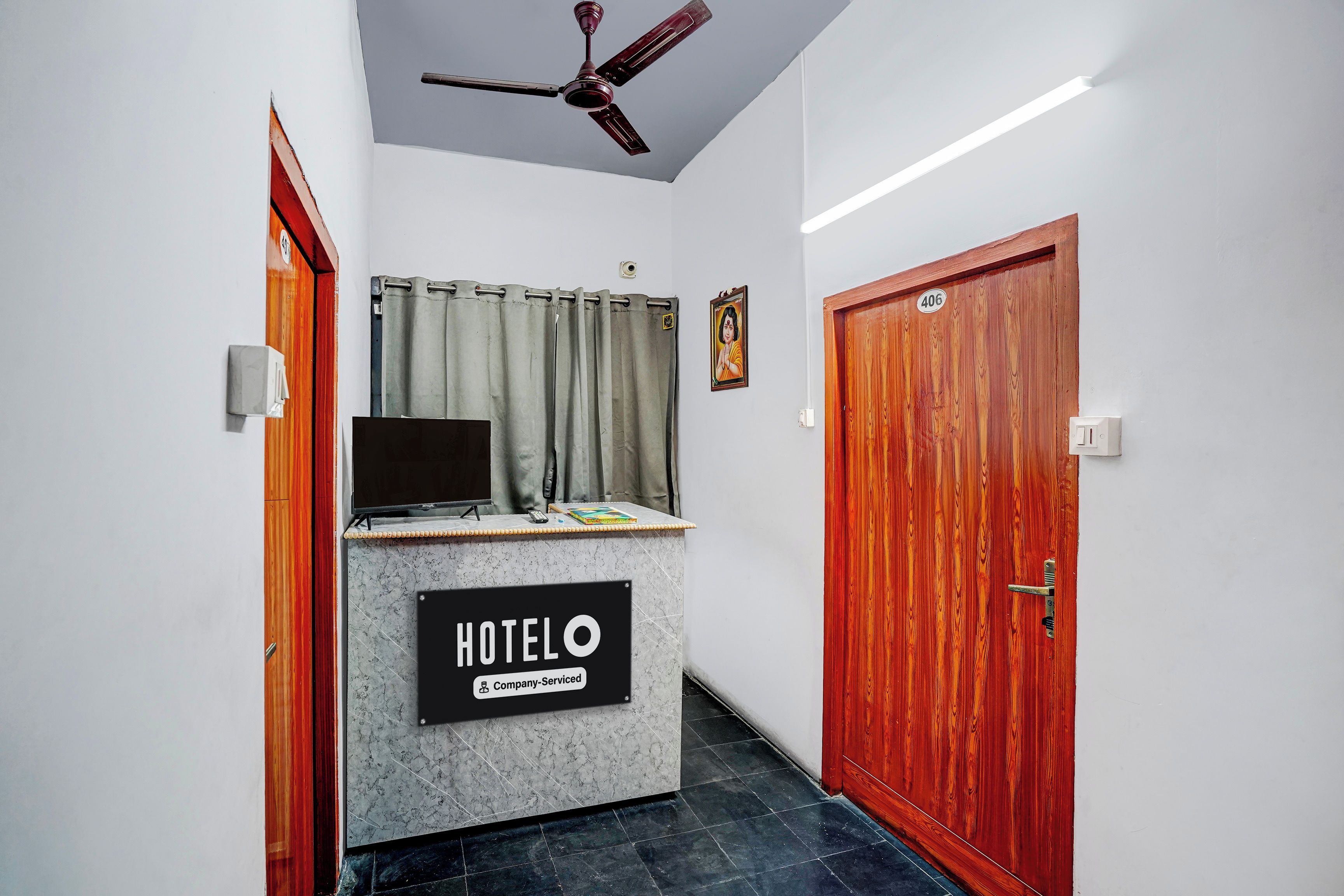 A hotel reception desk with a sign indicating it's company-serviced, a ceiling fan, a door with a number, and a curtain.