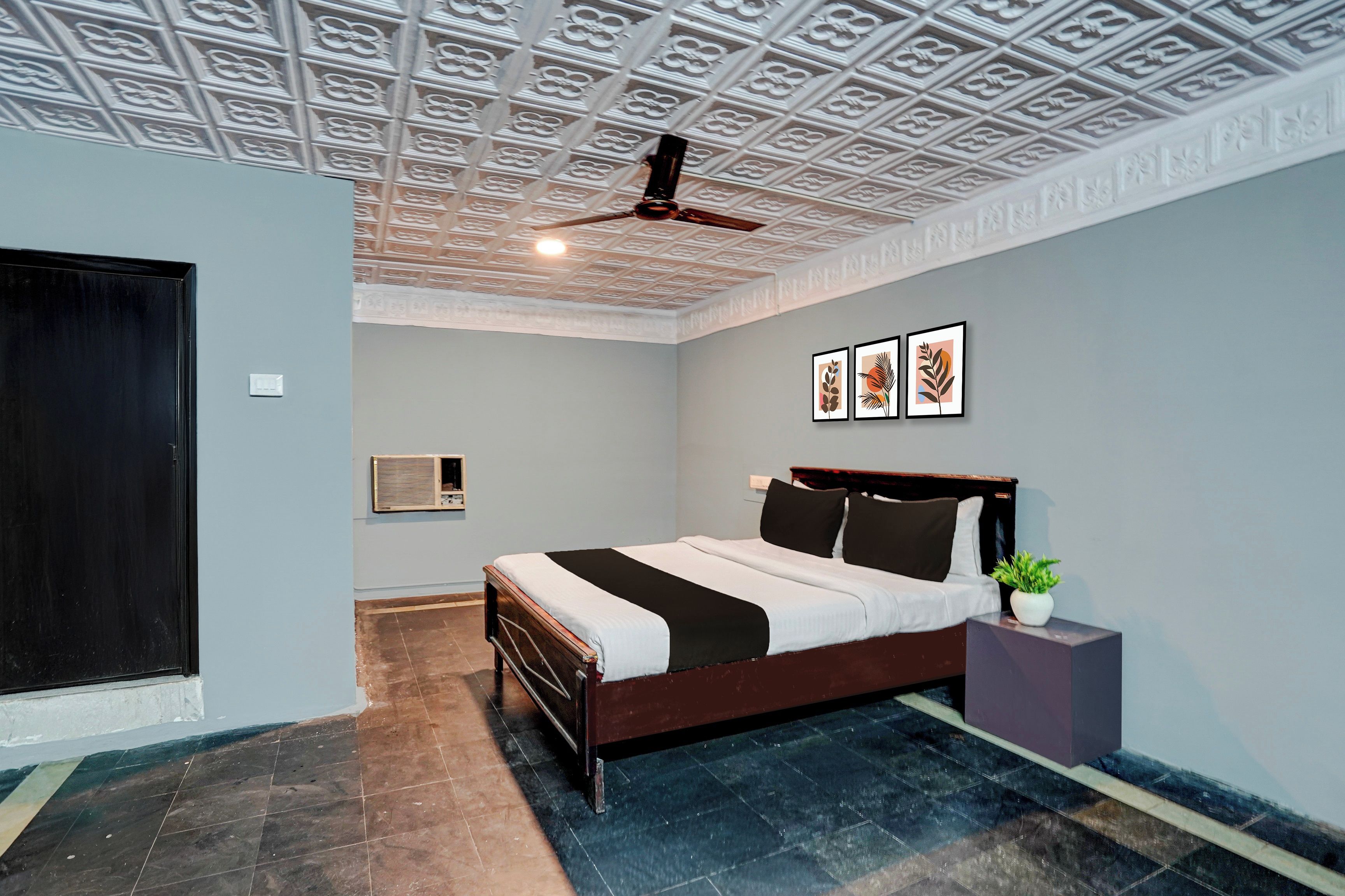A bedroom with a bed, a ceiling fan, a wall-mounted air conditioner, and three framed pictures.