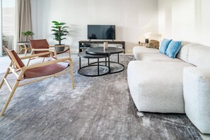 Un salon moderne comprenant un canapé, deux fauteuils, une table basse, un téléviseur et une plante en pot.