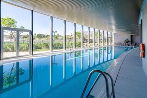 Une piscine intérieure avec des parois en verre transparent, une bouée de sauvetage et une vue sur l’extérieur.