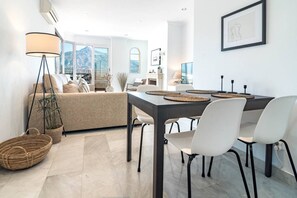 A modern living room with a sofa, a dining table with chairs, a lamp, and a view of mountains through large windows. - SAm24I- Cozy apartment walking distance to beach (Marbella)