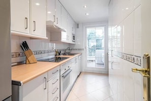 Une cuisine moderne avec des meubles blancs, un plan de travail en bois et une vue sur l’extérieur.